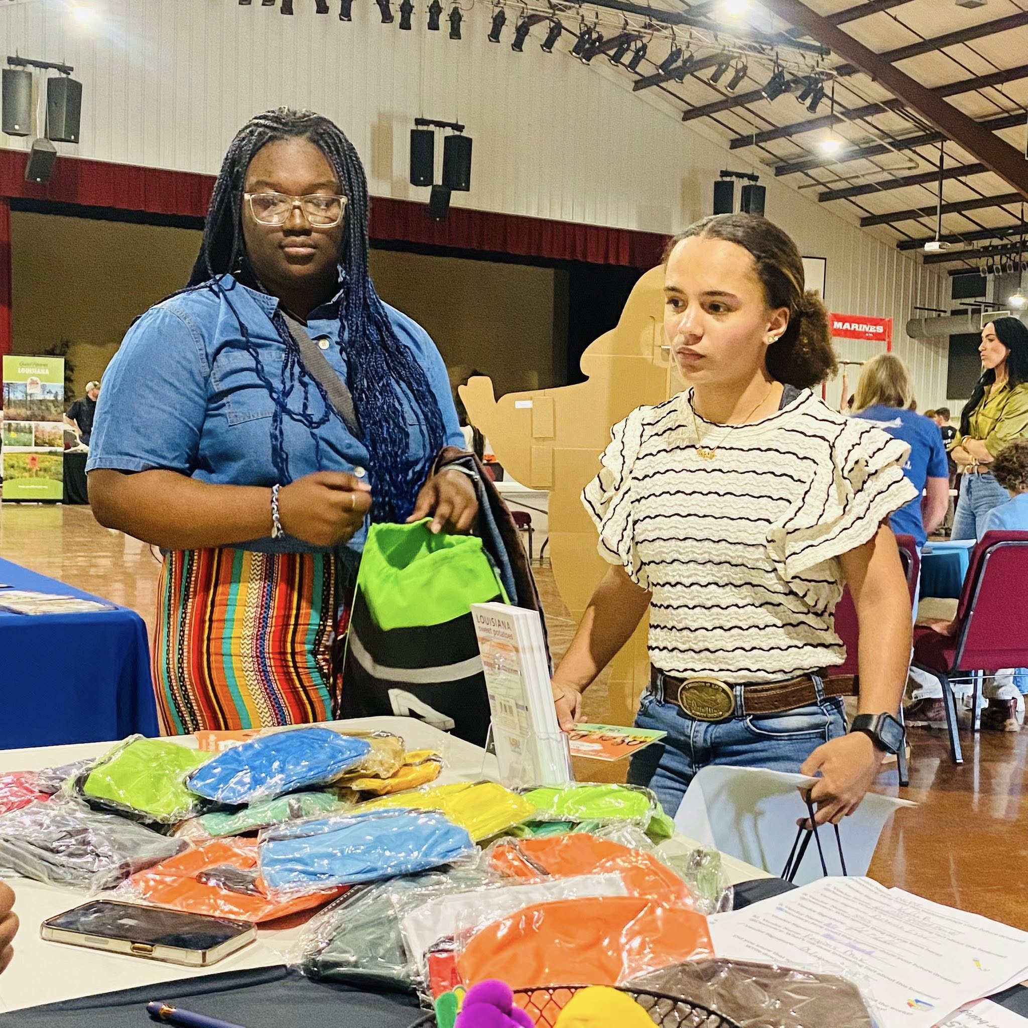 Two teen girls looking at stuff on a table.